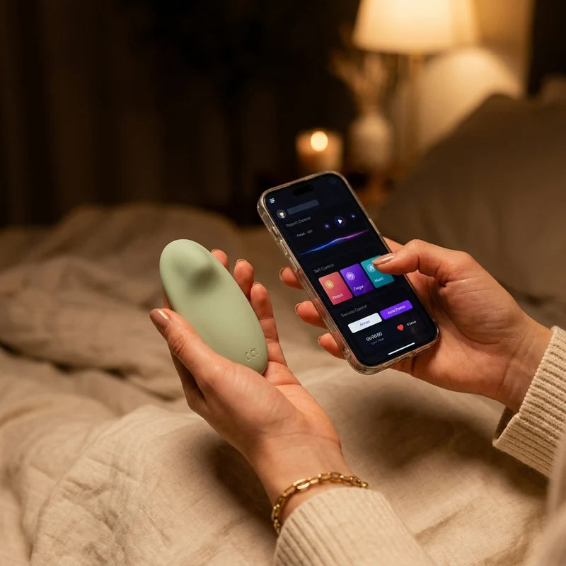 Hands holding the green-sage Petal Nyx beside a phone running the control app, warm low-light bedroom — a stable, working connection